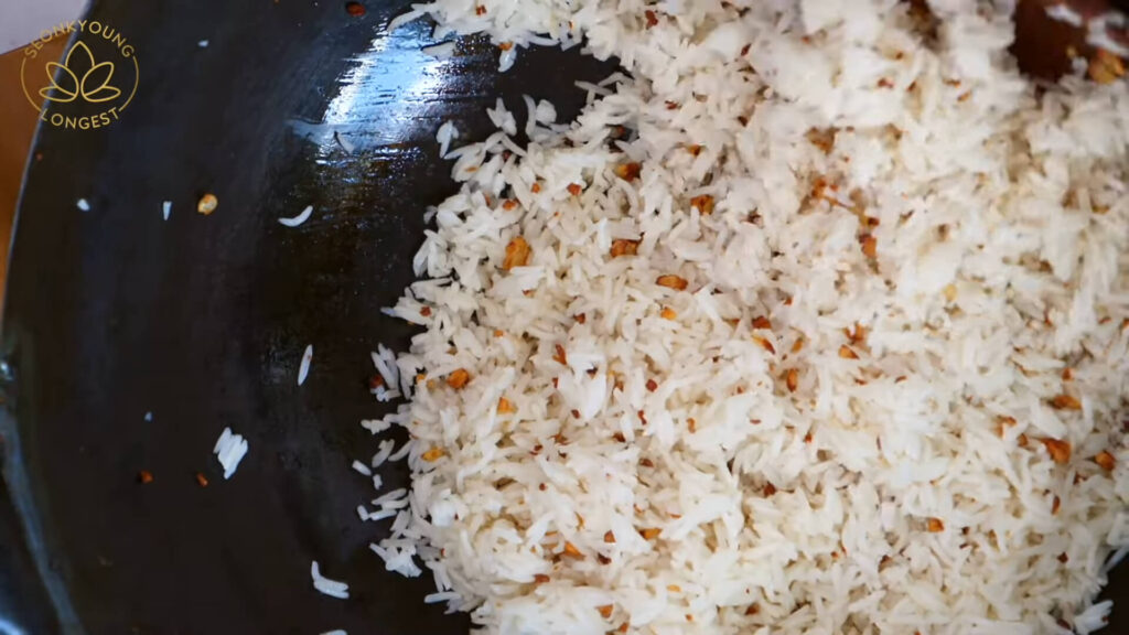 A close-up shot of golden garlic fried rice in a pan, glistening with oil and garnished with green onions.